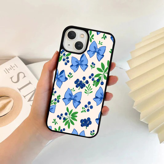 Phone case with a cream background featuring a pattern of blue ribbon bows, blueberries, and green leaves.